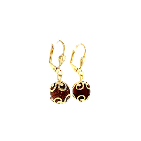The Adorned Goldstone Beads Drop Earrings, crafted with 14k gold-filled materials, feature stunning round goldstone beads encased in intricate filigree designs. Lead and nickel-free, they are ideal for sensitive skin and elegantly displayed against a crisp white background.